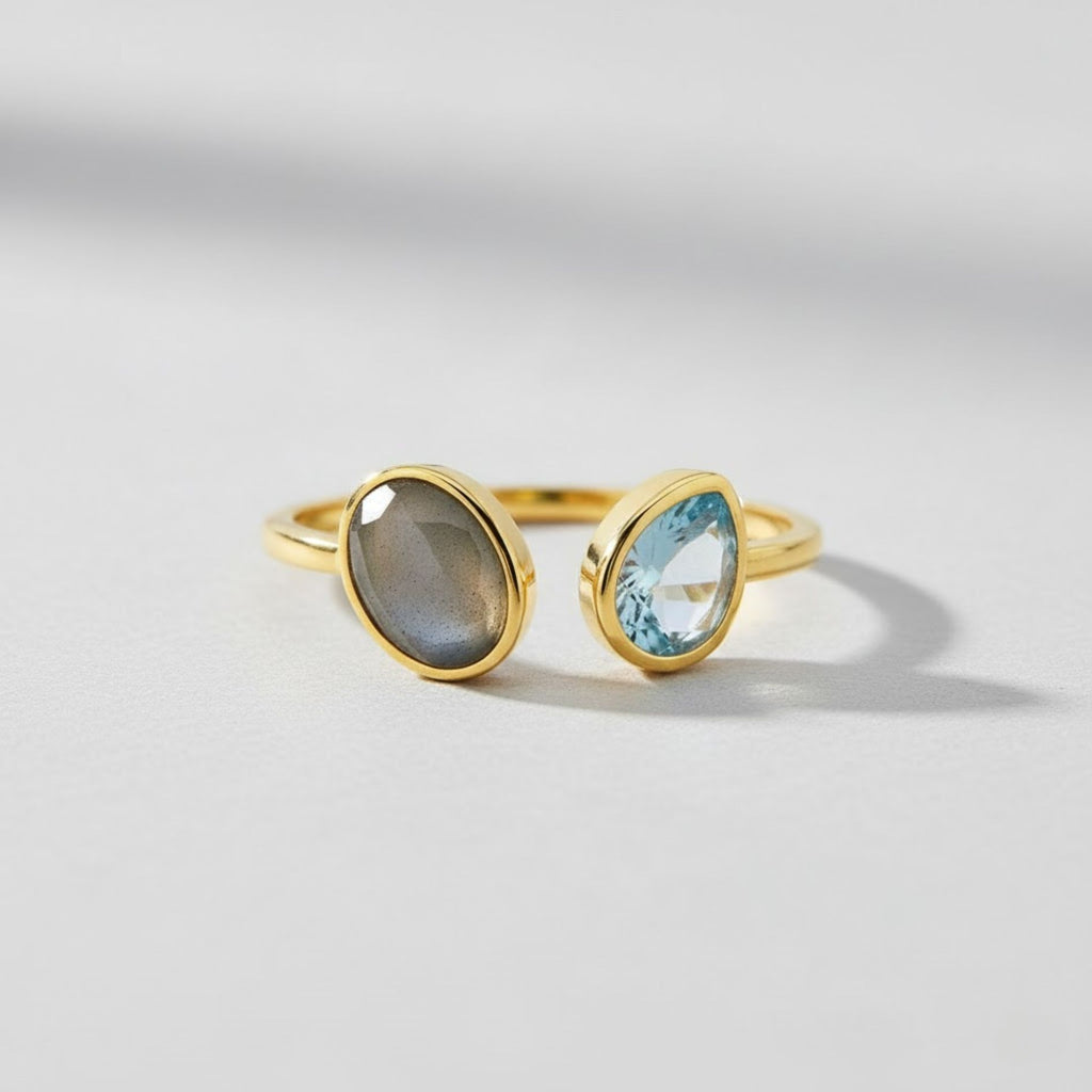Gold ring with a gray stone and a blue stone on a light gray background