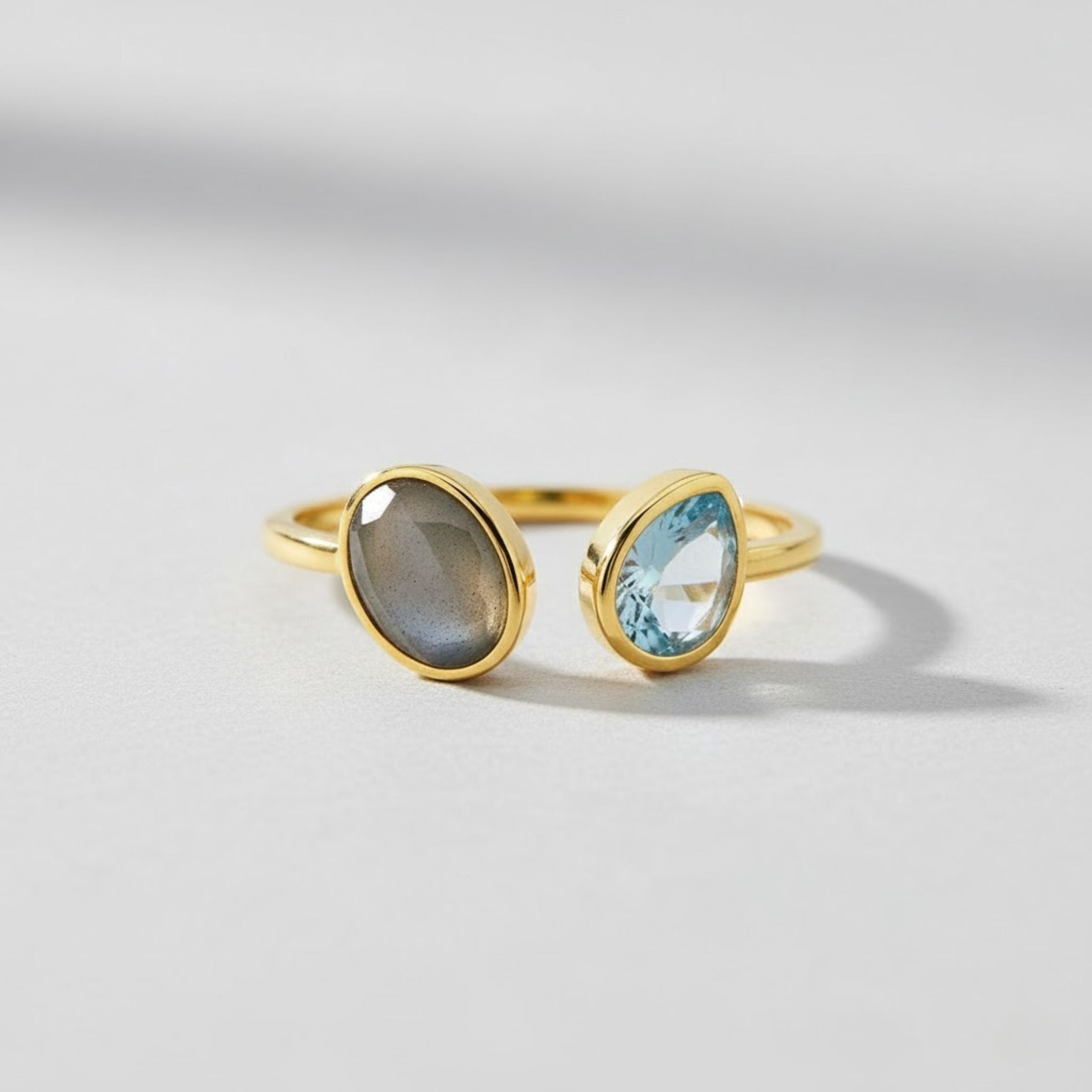 Gold ring with a gray stone and a blue stone on a light gray background