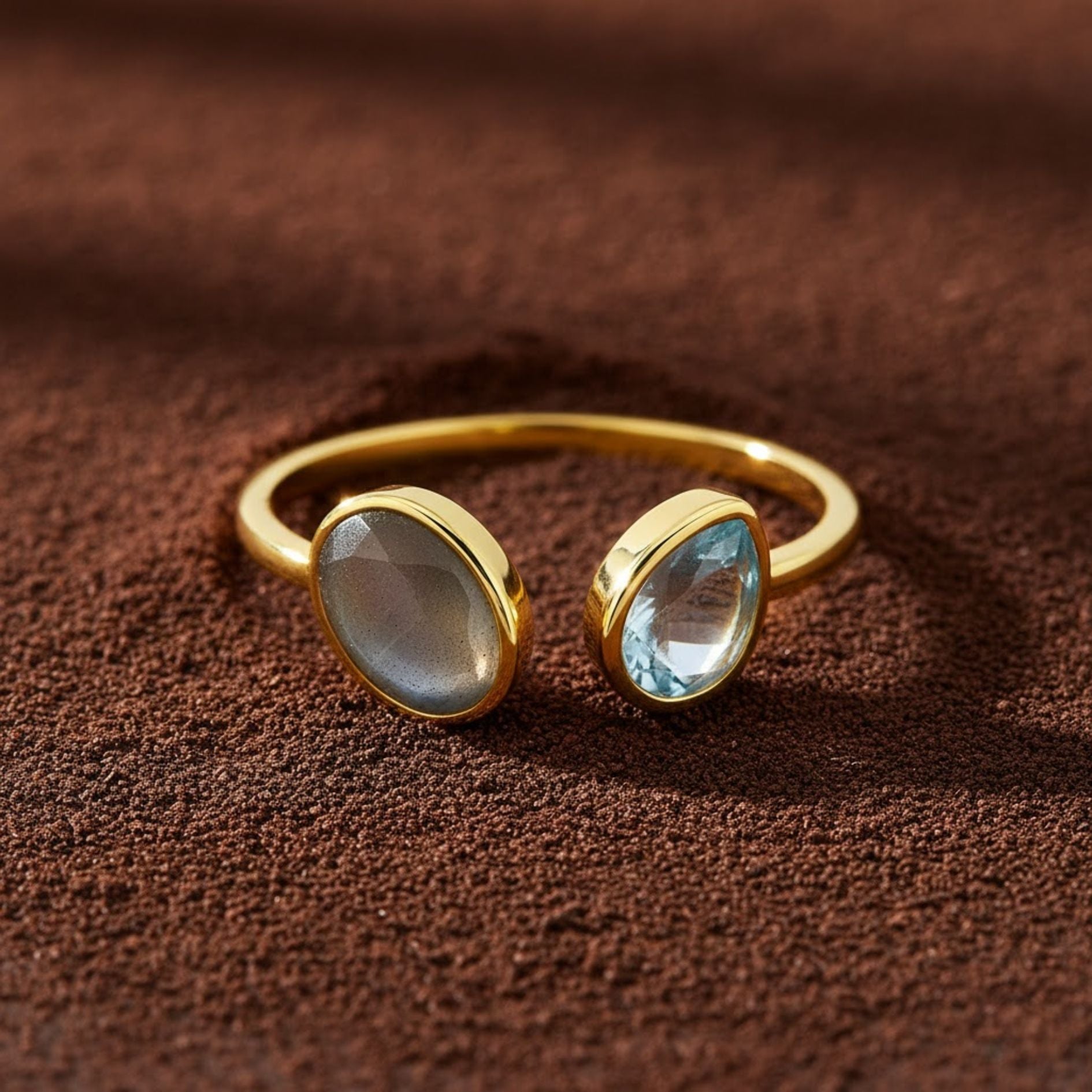 Gold ring with two gemstones on a brown textured background